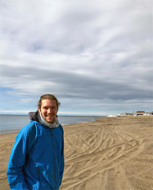 BCL/JD student David d'Astous standing on a northern beach near a village.